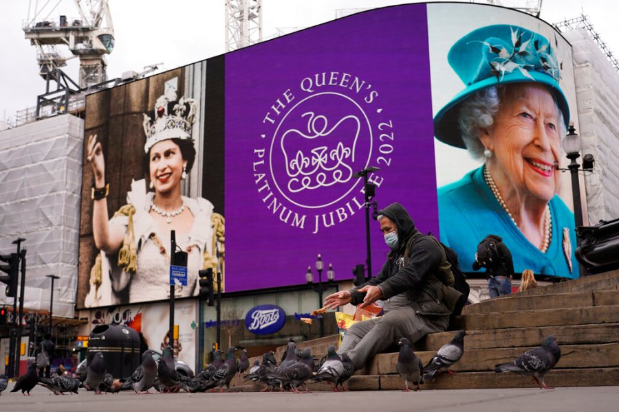 A man wears a face mask while he feeds birds, as the screen in Piccadilly Circus is lit to celebrate the 70th anniversary of Britain's Queen Elizabeth's accession to the throne, in London, Sunday, Feb. 6, 2022.(AP Photo/Alberto Pezzali)